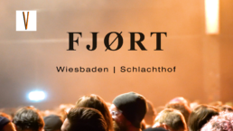 Schriftzug: FJØRT, darunter Wiesbaden | Schlachthof. Im Bild zu sehen sind Köpfe im Zuschauerraum mit orangenen Licht
