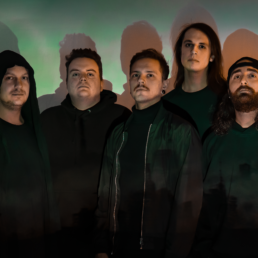 Leyka, Metalcoreband aus Mainz. 5 Männer in schwarzer Kleidung stehen in türkises Licht getaucht vor einer Wand