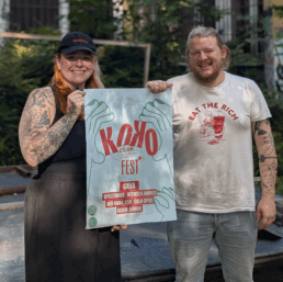 Hannah und Julius halten das Plakat hoch für das Jubiläumsfest des Konglomerat Kollektivs