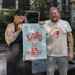 Hannah und Julius halten das Plakat hoch für das Jubiläumsfest des Konglomerat Kollektivs