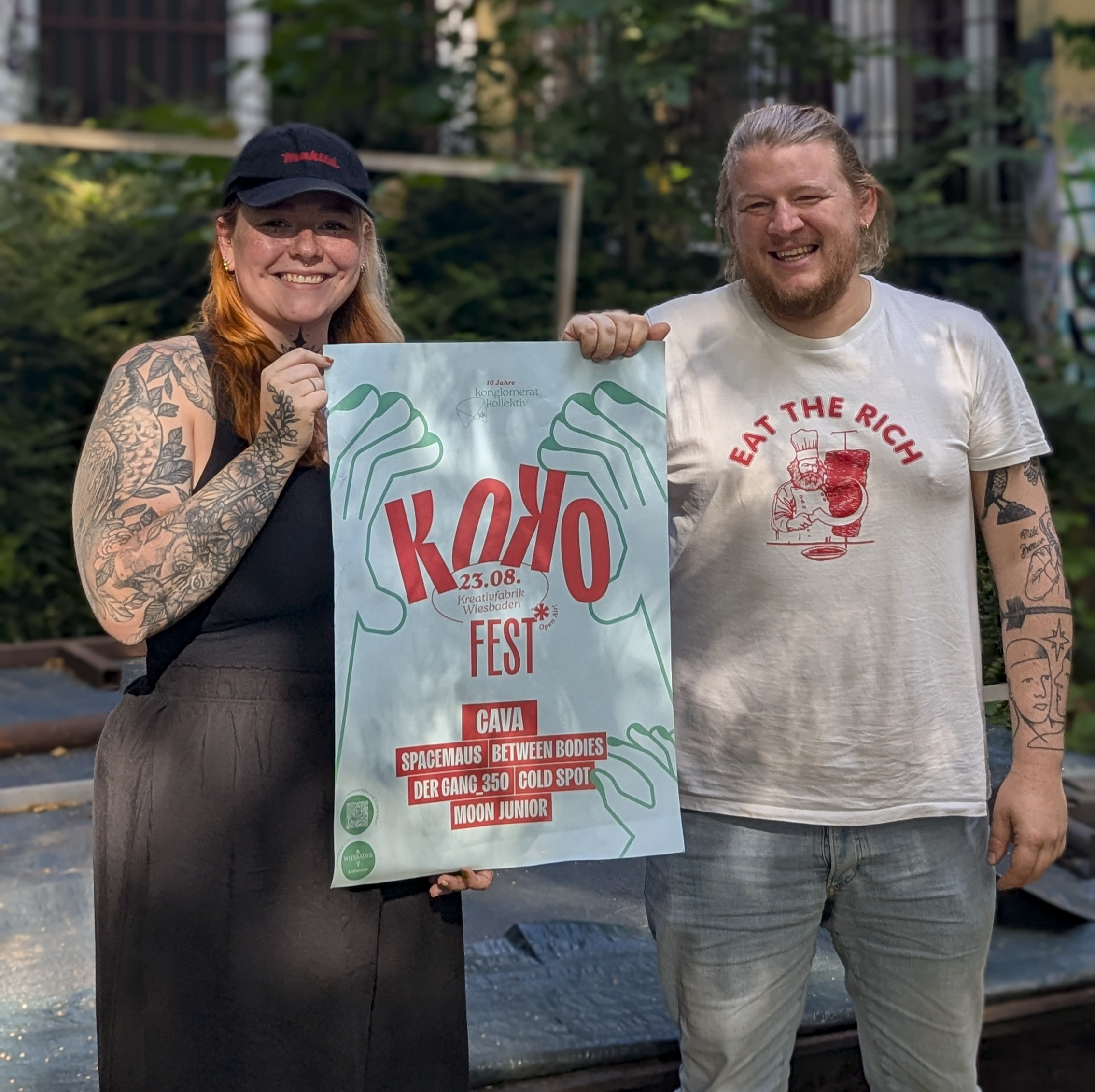 Hannah und Julius halten das Plakat hoch für das Jubiläumsfest des Konglomerat Kollektivs