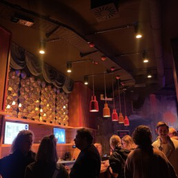 Eine von Menschen umringte Bartheke, die schwach durch von der Decke hängende Lampen beleuchtet wird.