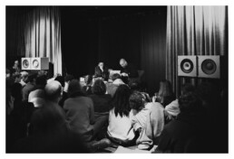 Schwarz-weiß-Bild von zwei Herren, die zu zweit auf einer Bühne Schallplatten vorstellen.