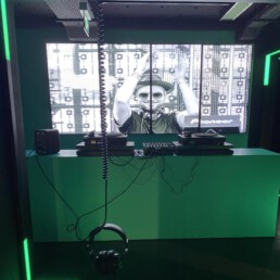 Ein grün beleuchtetes DJ-Pult mit davor hängenden Kopfhörern