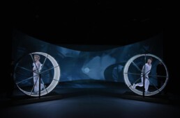 Zwei Schauspieler auf einer Bühne in jeweils einem Hamsterrad