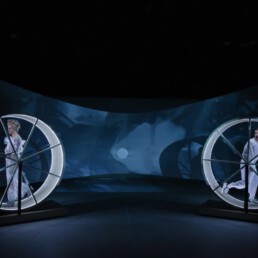 Zwei Schauspieler auf einer Bühne in jeweils einem Hamsterrad