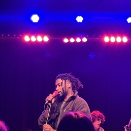 Der K&uuml;nstler Dews Pegahorn wird auf der B&uuml;hne von blauen und roten Lichtern angestrahlt.