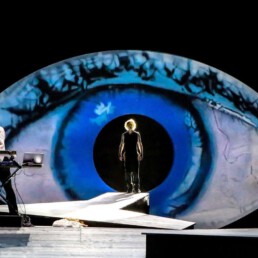 Eine Bühne mit zwei Personen, im Hintergrund ein riesiges blaues Auge