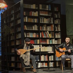 zwei Musiker auf einer Bühne vor einem großen Bücherregal